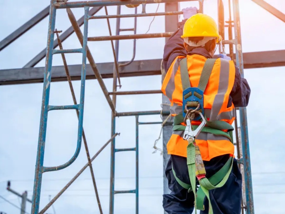 Worker in a full-body safety harness and high-visibility vest climbing scaffolding