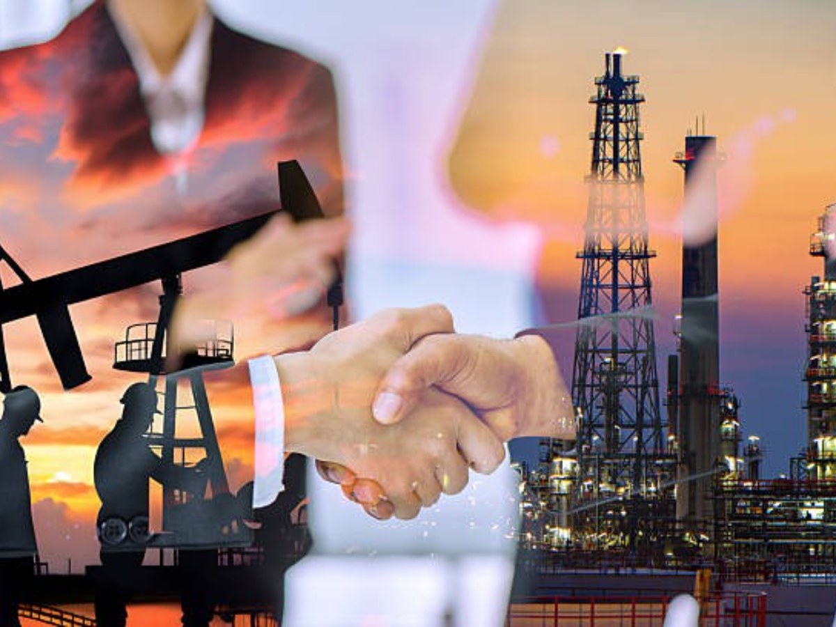 Handshake overlaid on oil field pump jacks and a refinery at sunset