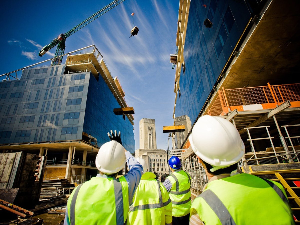 Site team in high-visibility vests watching a tower crane lift a steel beam
